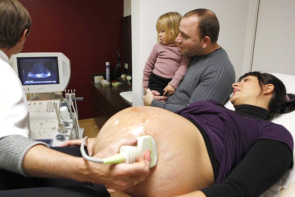 Pregnant woman getting ultrasound with husband and daughter watching