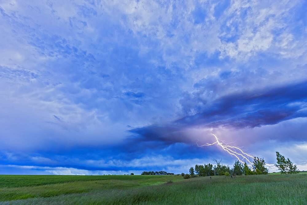 A lightning bolt comes out of a retreating thunderstorm, in the darkening twilight.