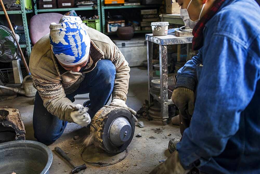 Takahiro Koizumi is breaking the mold just  after solidifying the molten iron. He casts the first look at new iron teapot or tetsubin, nanbu tekki, Workshop of Koizumi family,craftsmen since 1659, Morioka, Iwate Prefecture, Japan