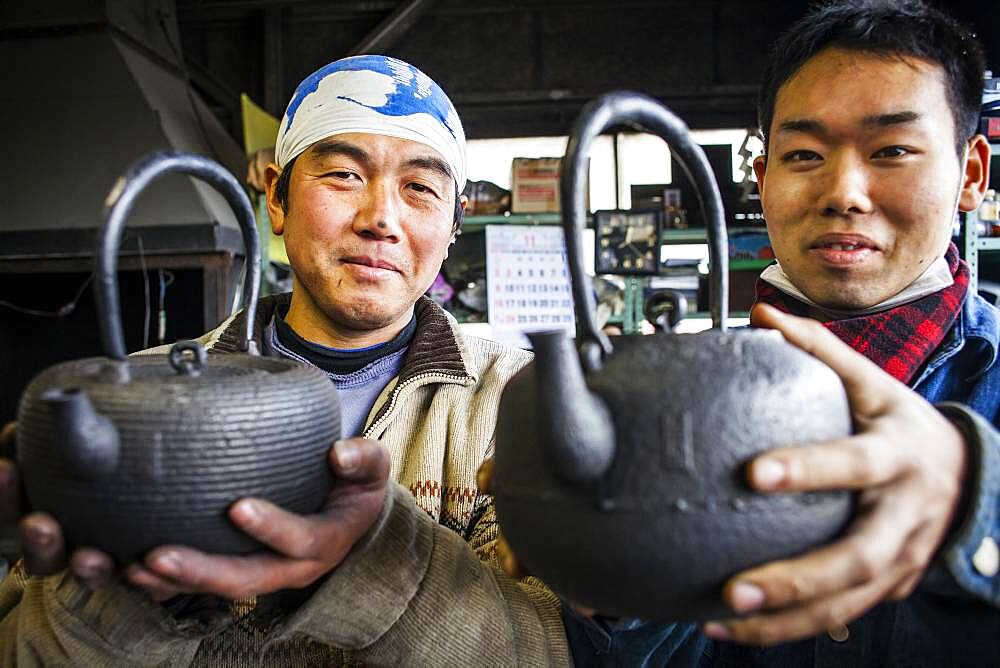 Takahiro Koizumi at left and his assistant Kohei ishimori  at right  are showing their finish work, iron teapots or tetsubin, nanbu tekki,Workshop of Koizumi family,craftsmen since 1659, Morioka, Iwate Prefecture, Japan