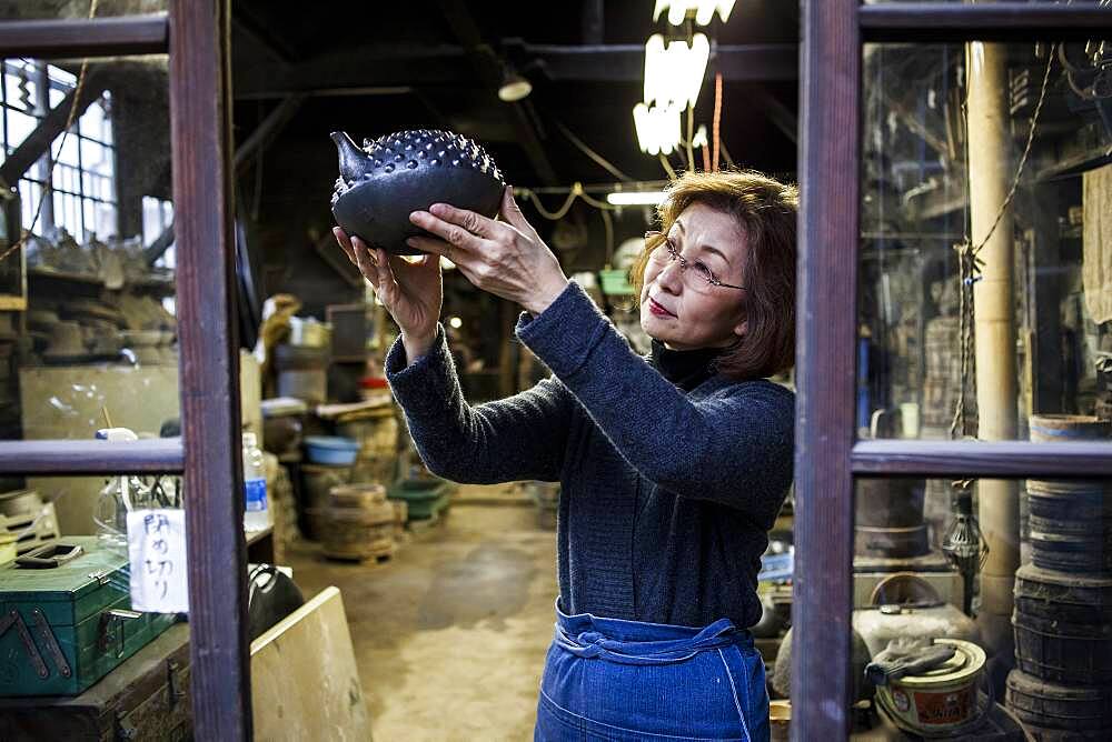 Morihisa Suzuki is reviewing the quality of work in a new iron teapot or tetsubin , the only woman who has made iron teapots in the nearly 400 years of history that has molten iron crafts in Iwate, in Workshop of Morihisha Suzuki,craftsmen since 1625, nanbu tekki, Morioka, Iwate Prefecture, Japan