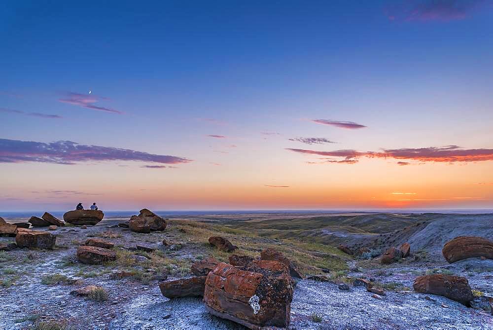 A pair of campers watch the sunset with the 4-day-old waxing Moon in the twilight sky above, at Red Rock Coulee in southeast Alberta.