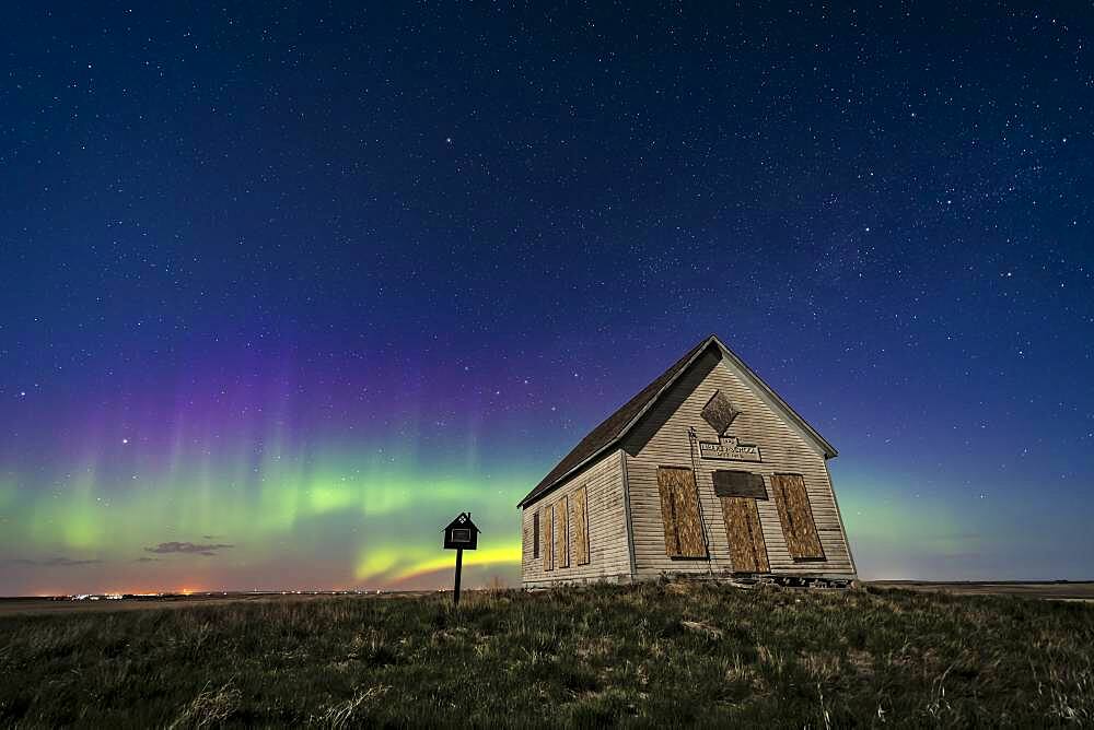 The 1910 Liberty Schoolhouse, a classic pioneer one-room school, on the Alberta prairie under the stars on a spring night, with an aurora dancing to the north. Moonlight provides the illumination. Cassiopeia is above the school. Polaris is at top.