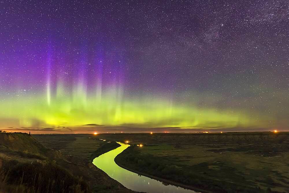 The Northern Lights dance over the sweeping Red Deer River and Badlands of southern Alberta, from Orkney Viewpoint looking north over the valley. The Bleriot Ferry crossing is in the distance at the lights. Cassiopeia is embedded in the purple curtains. The river reflects the aurora light.