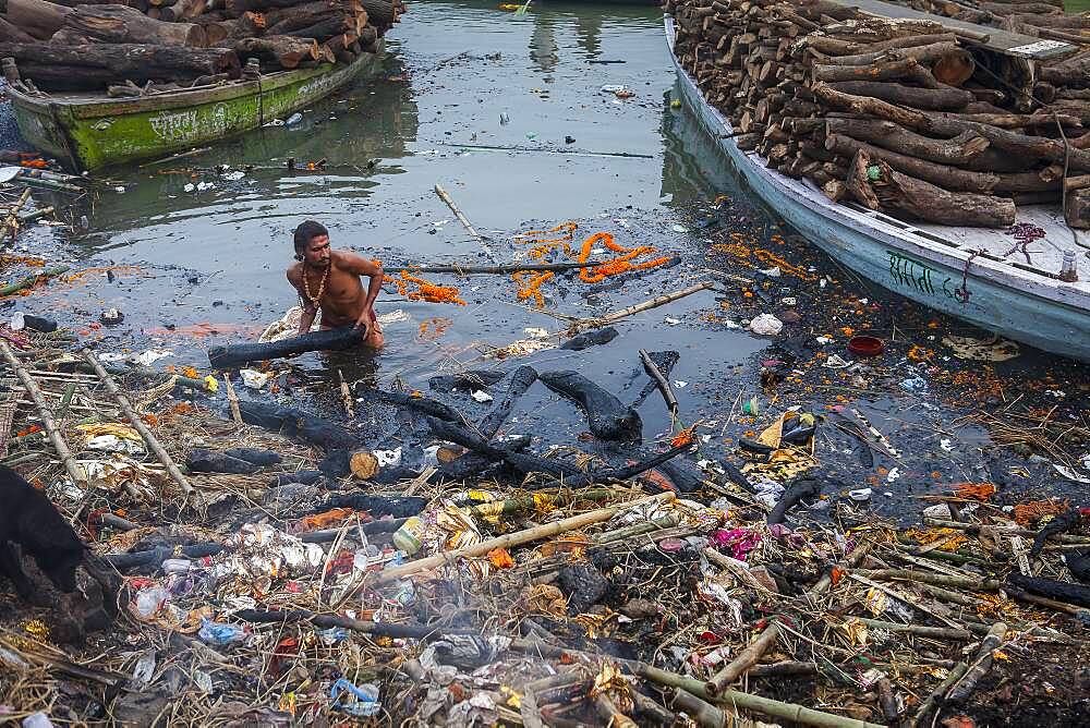 Person who recovers wood used in cremation, which has not burned completely, in Manikarnika Ghat, the burning ghat, on the banks of Ganges river, Varanasi, Uttar Pradesh, India.