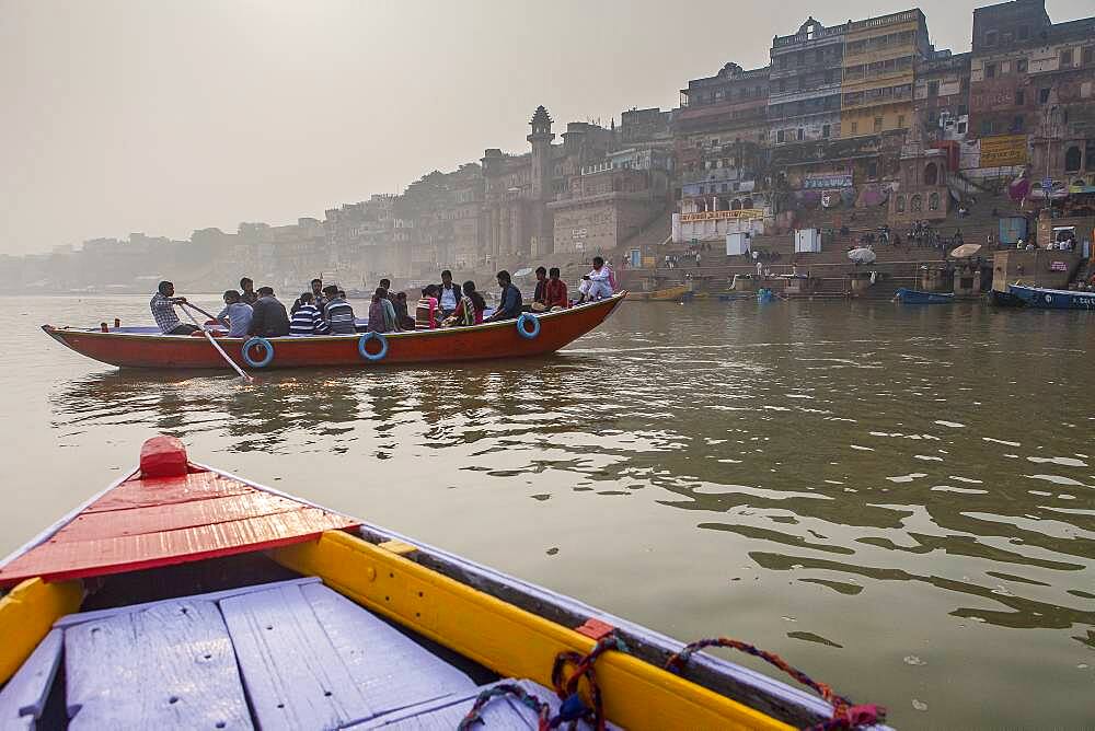 Pilgrims in a boat sailing and praying, Ganges river, in background the ghats, Varanasi, Uttar Pradesh, India.