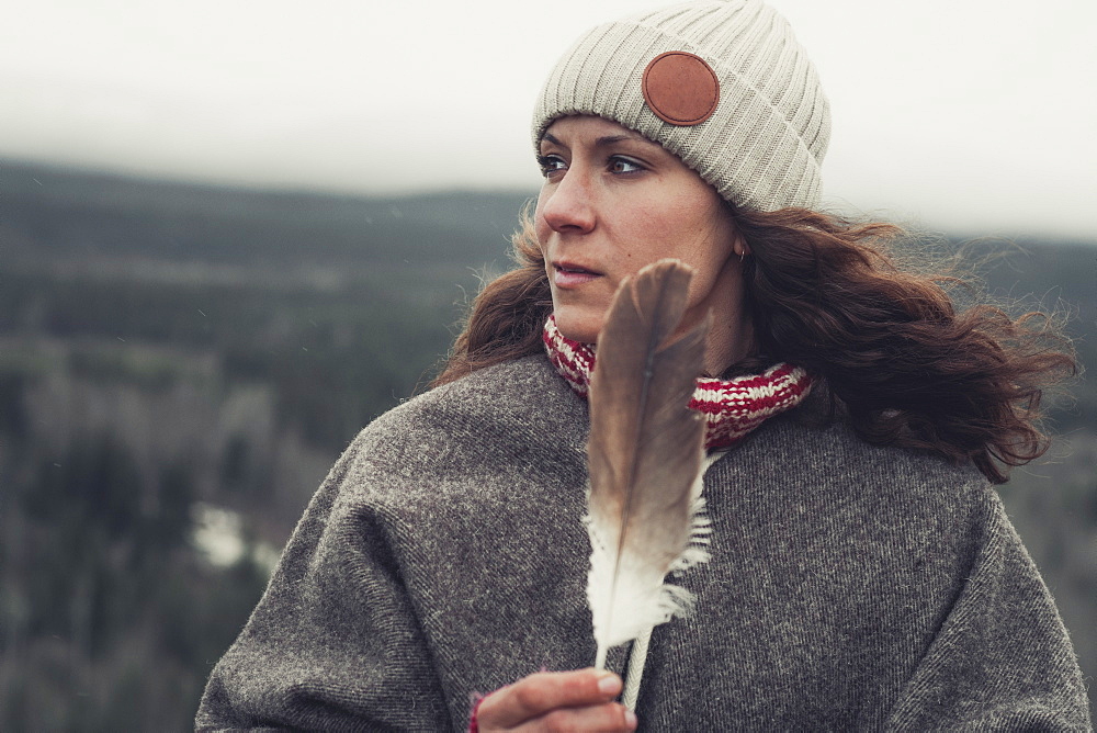 An attractive brunette holds an eagle's feather in her hands and alooks over the land. Yukon Territory, Canada