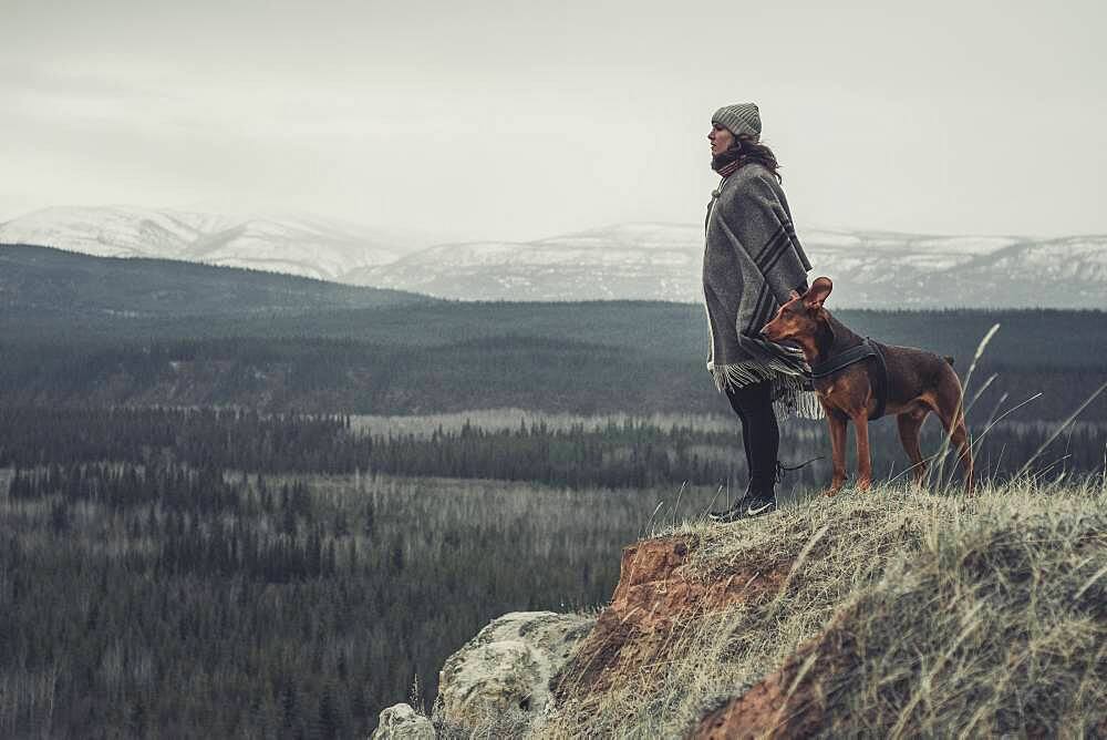 A young Woman is enjoying the view over the land togehter with her dog. Yukon Territory, Canada