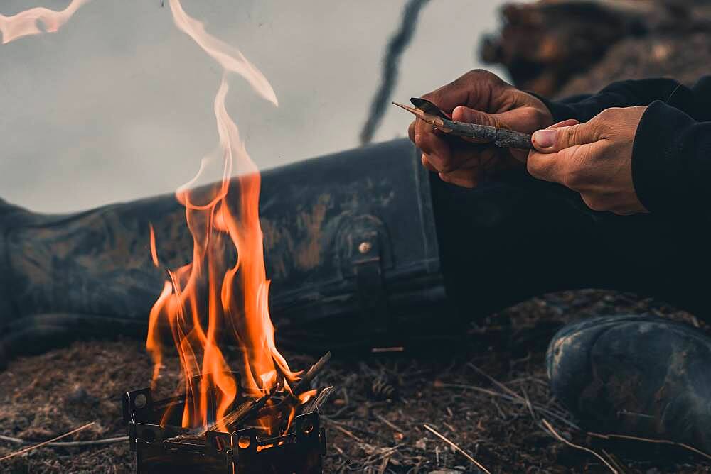 Woman carving a stick to cook over the campfire. Yukon Territory, Canada