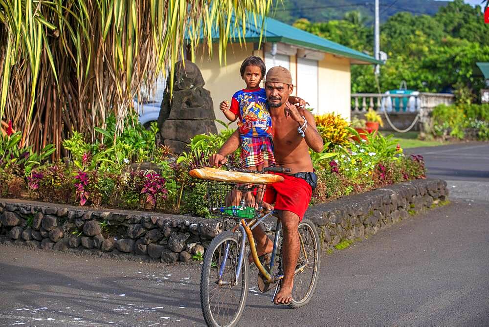 Tahitian man with her daughter carrying baguettes while riding a bicycle on the island of Tahiti, French Polynesia, Tahiti Nui, Society Islands, French Polynesia, South Pacific.