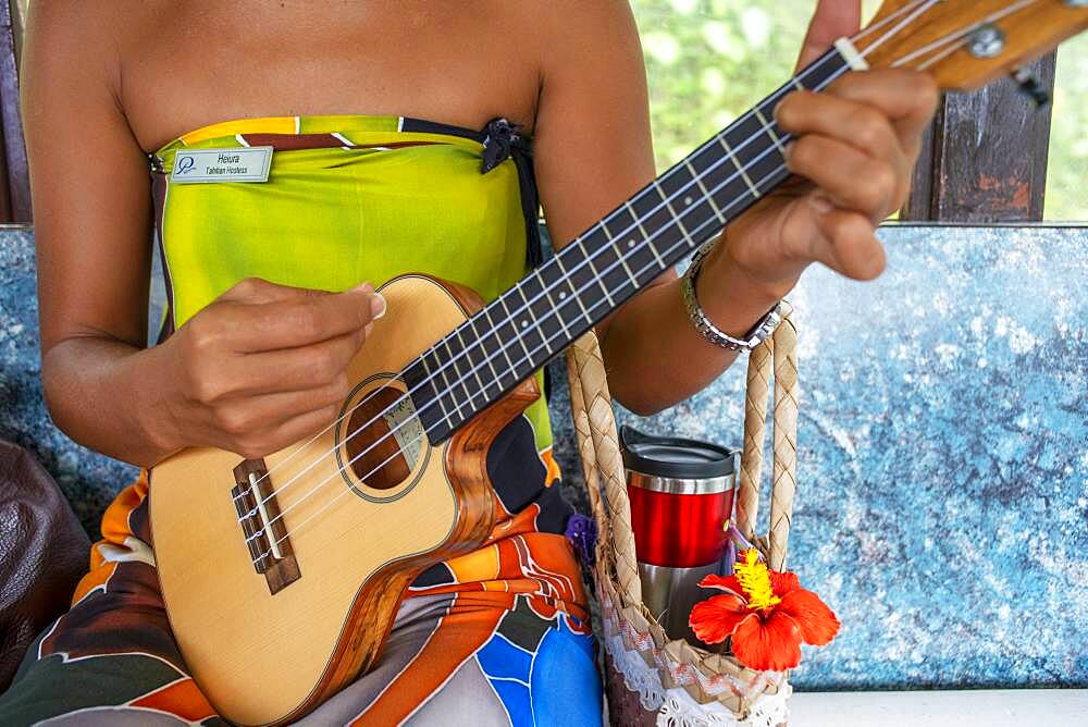 Beautiful local woman playing ukulele in Huahine island, Society Islands, French Polynesia, South Pacific.   Coastline and lagoon of Huahine island near Maroe bay, south Pacific ocean, OceaniaSouth Pacific.