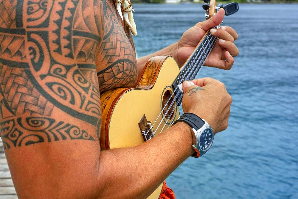 Local tattooed person playing the ukulele in Huahine, Society Islands, French Polynesia, South Pacific.