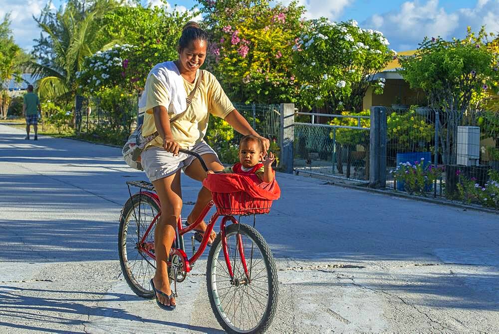 Local girl with a bike and small child in Fakarava,  Tuamotus Archipelago French Polynesia, Tuamotu Islands, South Pacific.