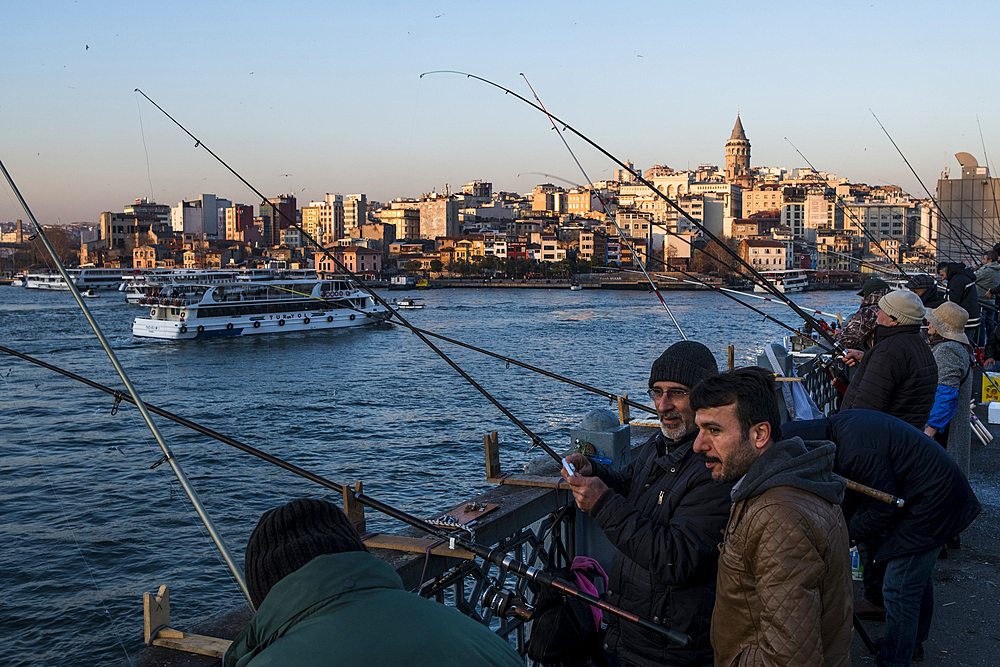 People fishing from Galata Bridge in front of Galata neighbourhood and Galata Tower during sunset in the Golden Horn