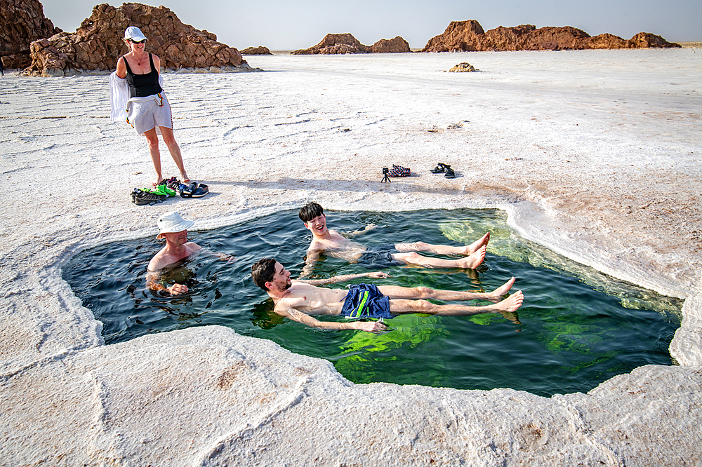 Tourists relax inside the water of Lake Karum, visible through a hole in the salt flat, Danakil Depression, Ethiopia.