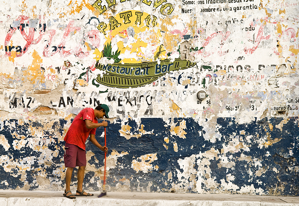 Man sweeping sidewalk and faded signs on wall, Avenida Zaragoza, old town Mazatlan, Mexico.