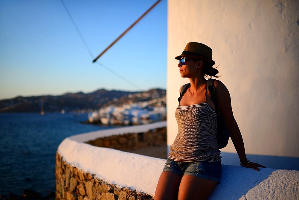 Young woman enjoying sunset from traditional windmills (Kato Milli) in Mykonos town, Greece