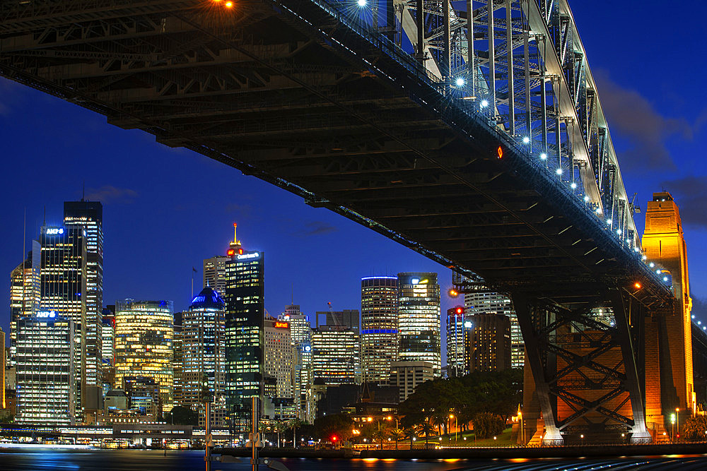 Side view of Sydney Harbour bridge architectural landmark and city at sunset. Illuminated arch of the bridge reflecting in blurred waters Sydney, New South Wales, Australia