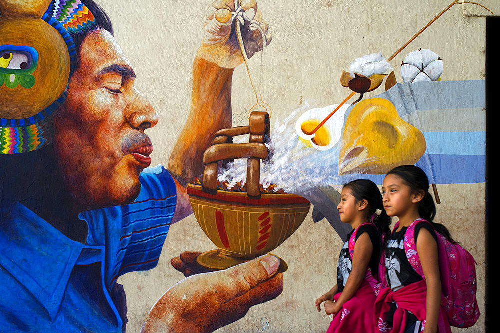 Two girs walking in front of a wall panting in San Juan La Laguna, Solol√°, Guatemala. Traditional mayan painting art Santiago Atitlan, lake Atitlan, Guatemala.