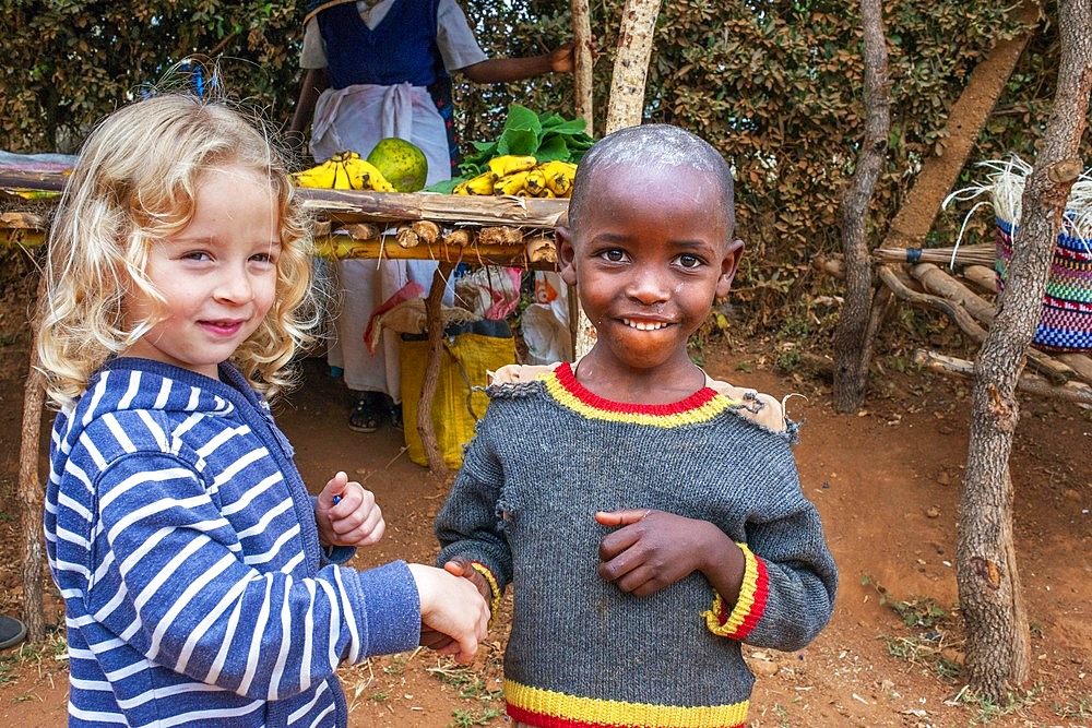 European blonde girl giving the hand and sharing with a black children boy in the primary and second school in a small village near Kitui city in the Kamba country in Kenya, Africa.