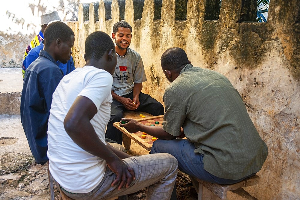 Group of Musilm men playing carrom, wearing traditional clothes enjoy leisure time in Lamu island town