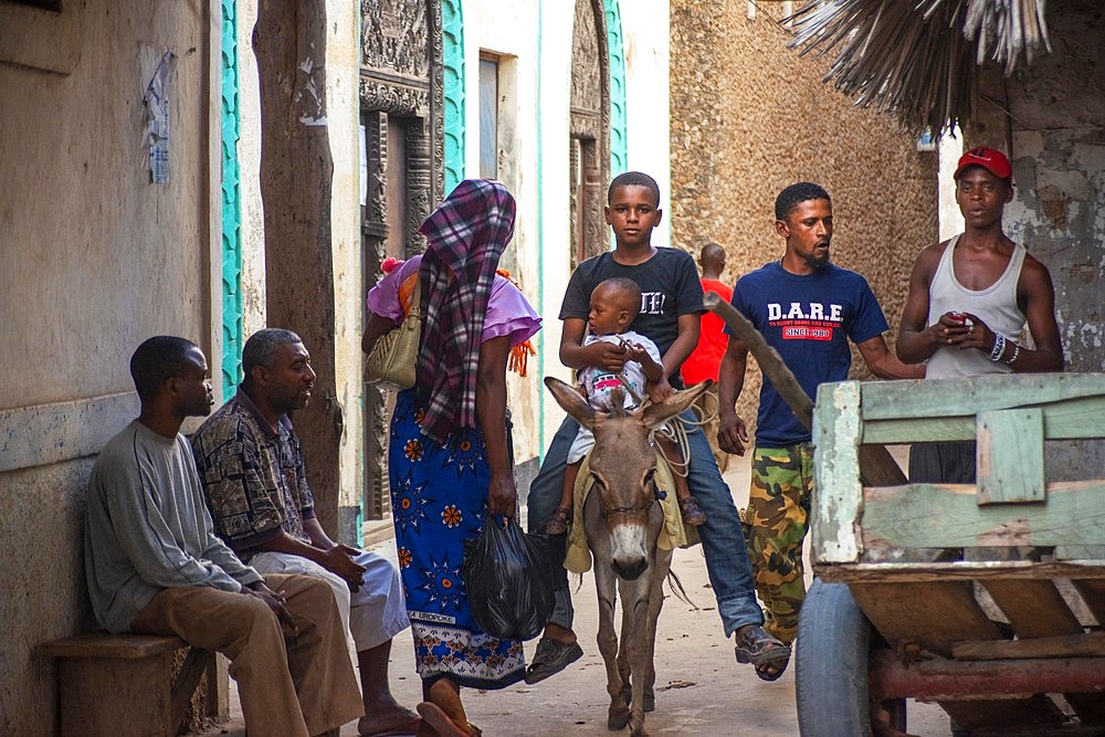 Men riding donkeys on the main street of Lamu town in Lamu Island, Kenya.