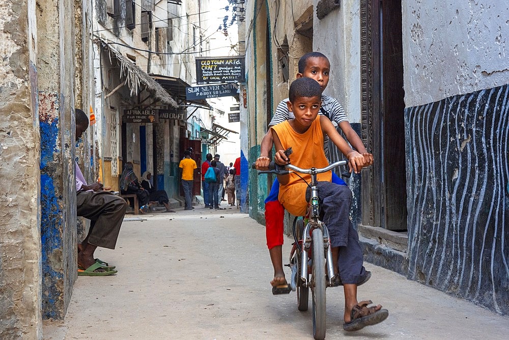 Boys riding on a bicycle in a narrow street of Lamu town in Lamu Island, Kenya.