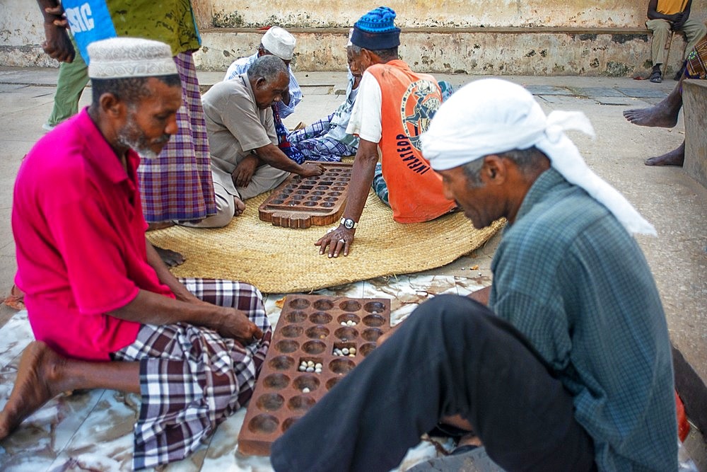 Group of Musilm men playing awale or Bao wearing traditional clothes enjoy leisure time in Lamu island town