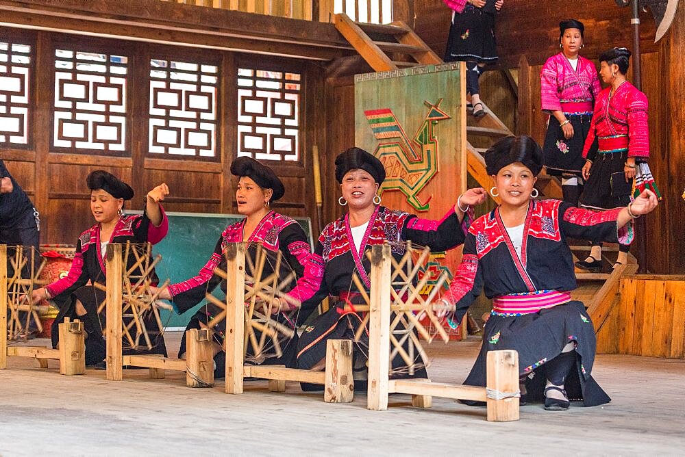 Red Yao ethnic minority women demonstrate spinning thread for weaving their traditional blouses. Huangluo, China.