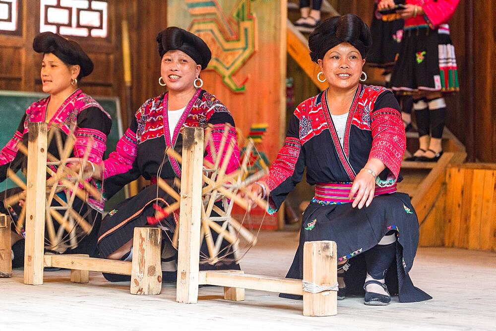 Red Yao ethnic minority women demonstrate spinning thread for weaving their traditional blouses. Huangluo, China.