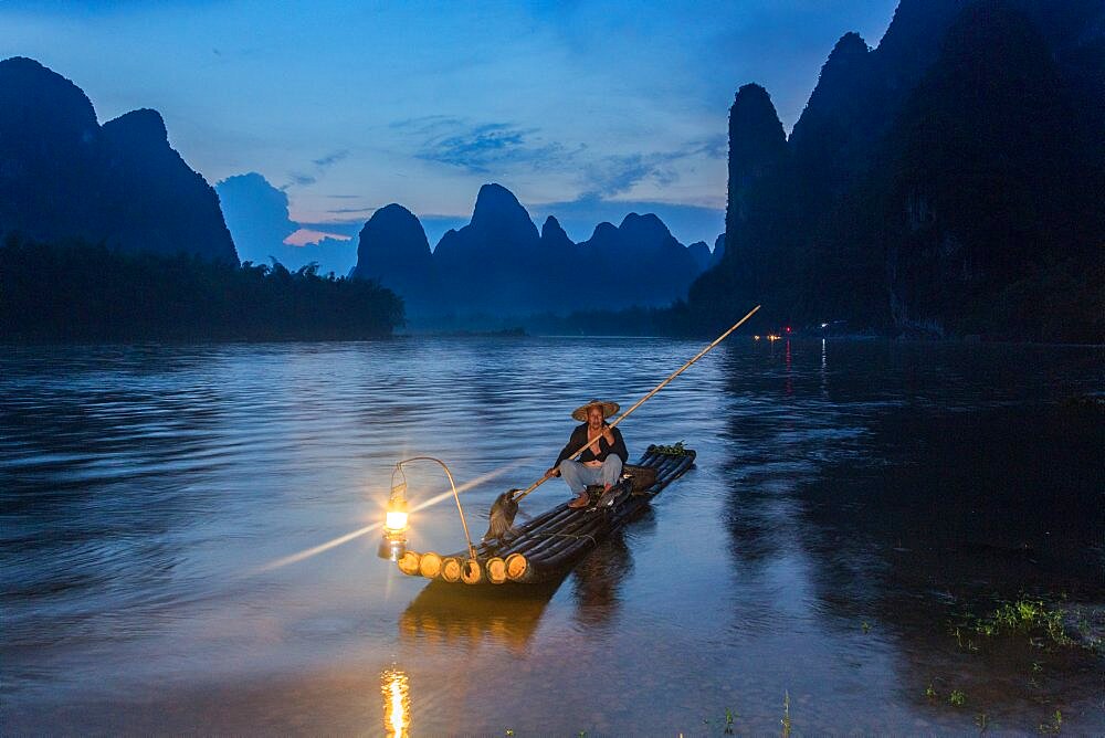 A traditional cormorant fisherman on a bamboo raft with his cormorants on the Li River, Xingping, China.