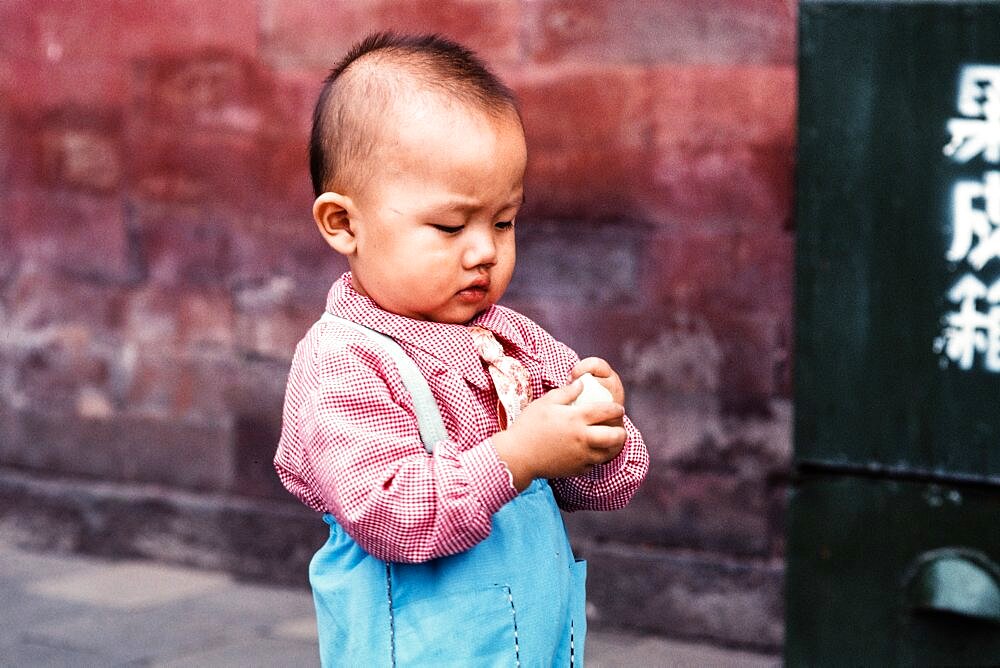 A young boy in a necktie opens a piece of candy on the street in Beijing, China.