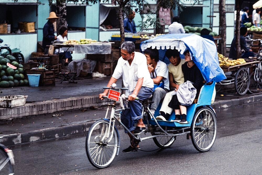 Chinese people riding in a tricycle pedicab or taxi on the streets of Beijing, China.