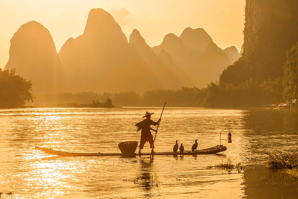 A cormorant fisherman poles his bamboo raft on the Li River iat sunset. Xingping, China.