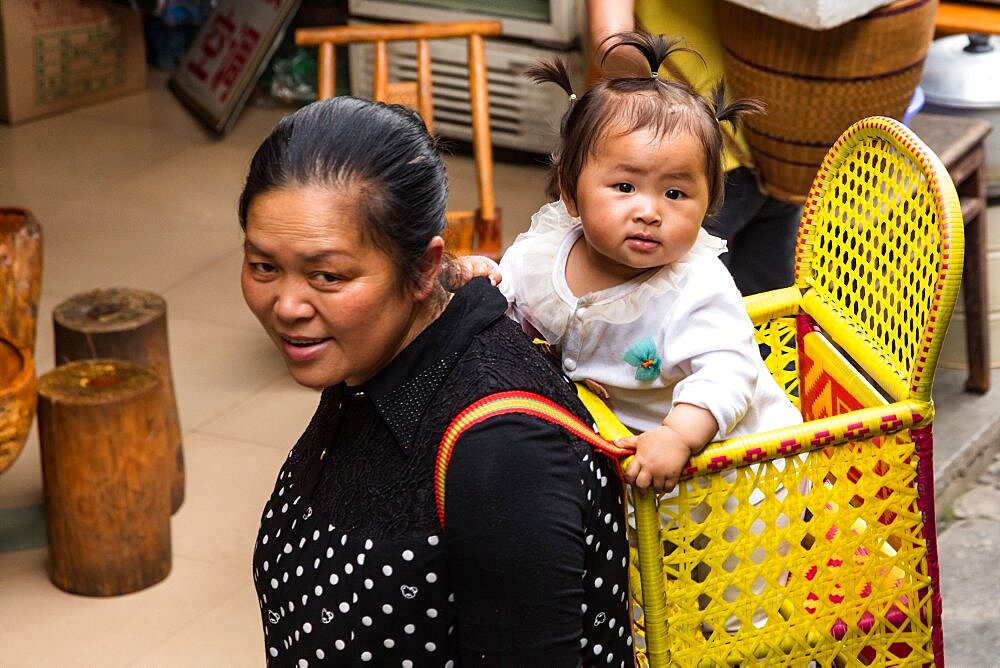 A Chinese mother carrying her baby daughter in a basket on her back in the ancient town of Furong, China.