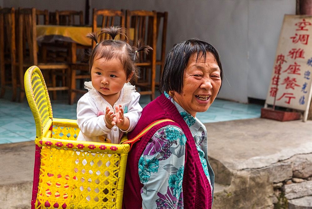 A Chinese grandmother carries her baby granddaughter in a basket on her back in Furong, China.