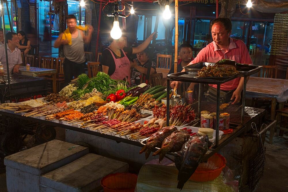 Food vendors with food for sale in the street market at night in the ancient town of Fenghuang, China.