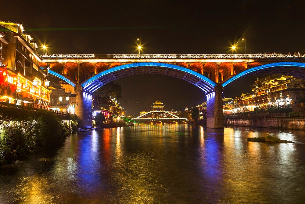 The hIghway bridge frames the Fenghuang Bridge lit up at night in Fenghuang, China.