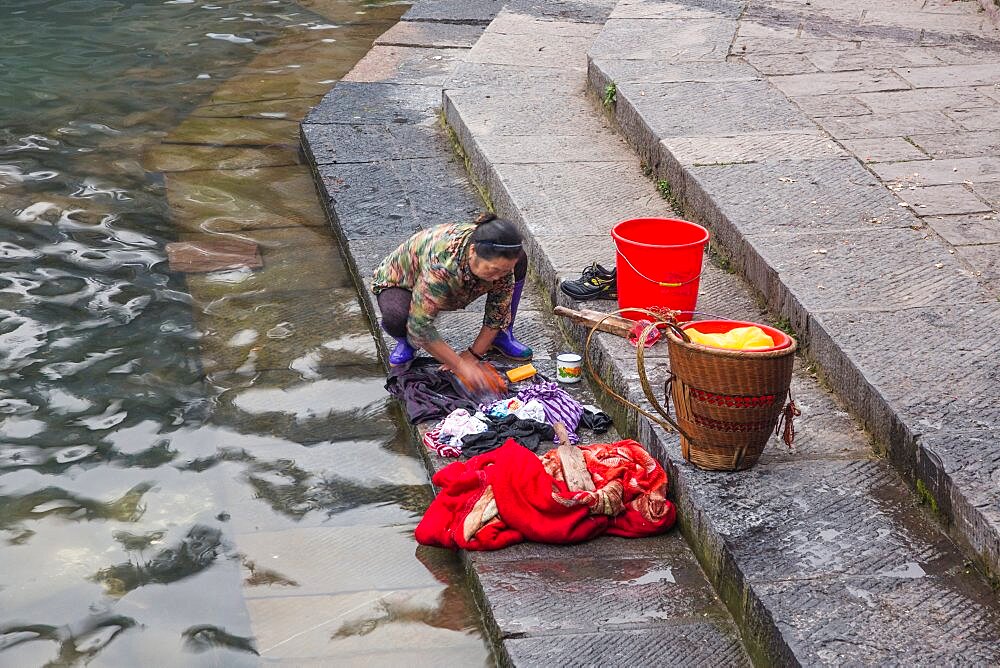 A Chinese woman washes laundry by hand on the steps into the Tuojiang River in Fenghuang, China.