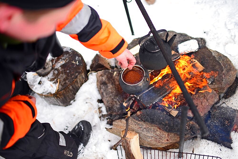 Antti, young guide from VisitInari, prepare coffee and tea on a fire in the wilderness of Lake Inari, Lapland, Finland