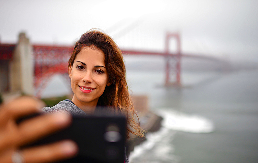 Young woman takes a selfie with Golden Gate Bridge, San Francisco,