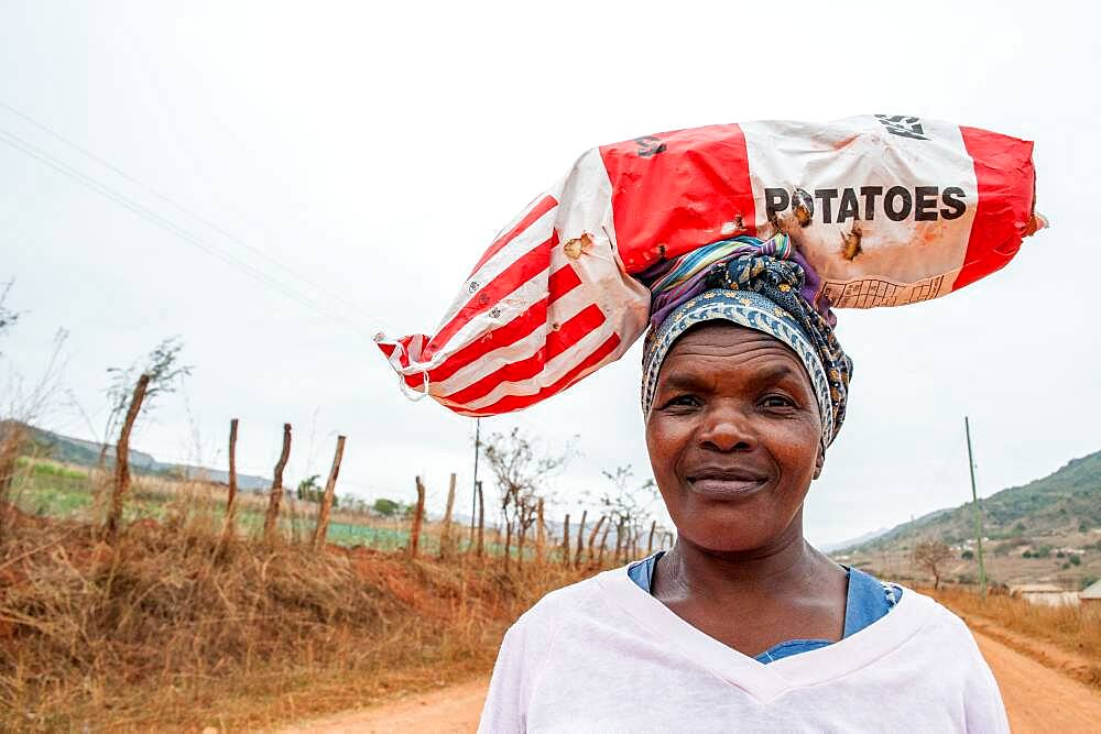 Woman carrying a bag of potatoes on her head down a dirt road in the Hhohho region of Swaziland, Africa.