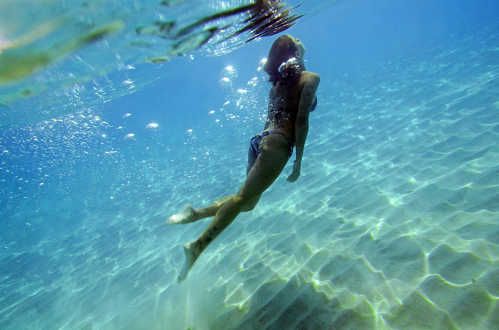 Young woman swims underwater in the beautiful waters of Menorca, Spain