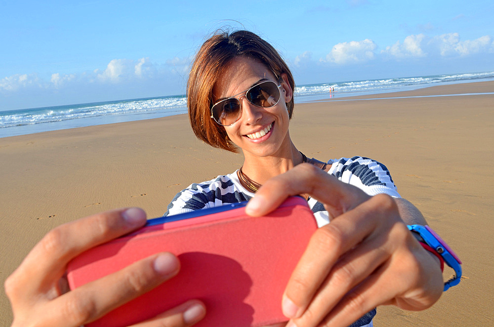 Attractive young woman on the beach, taking a selfie with mobile phone