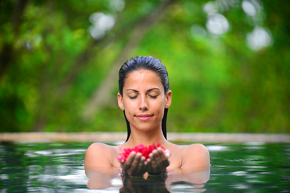 Young attractive woman holding red flowers in an infinity edge swimming pool, The Dutch House, Galle, Sri Lanka