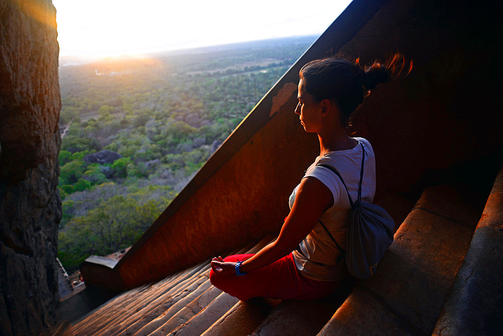 Young woman sits in lotus pose in the stairs up to the Ancient City of Sigiriya, Sri Lanka