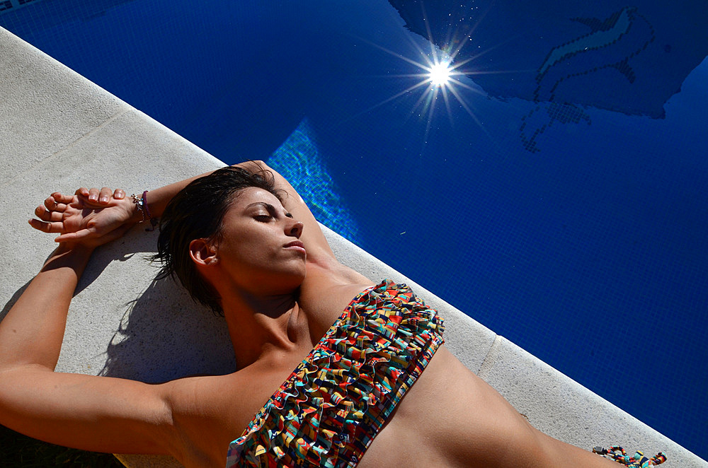 Attractive short haired woman sunbathing by the swimming pool