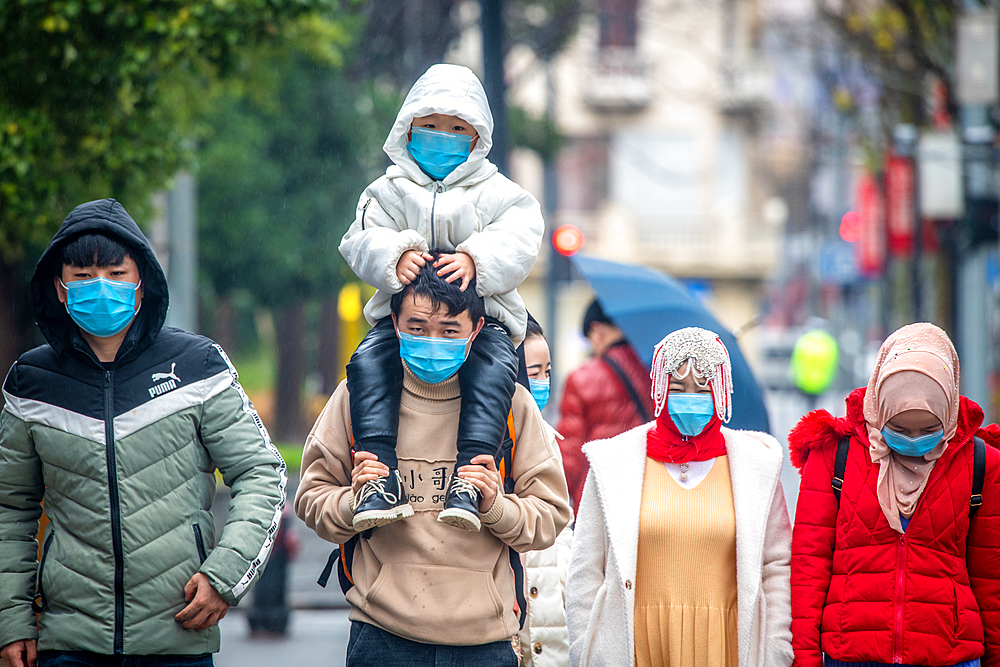 Shanghai, China, 25th Jan 2020, A group of people wearing masks walks down street on rainy day