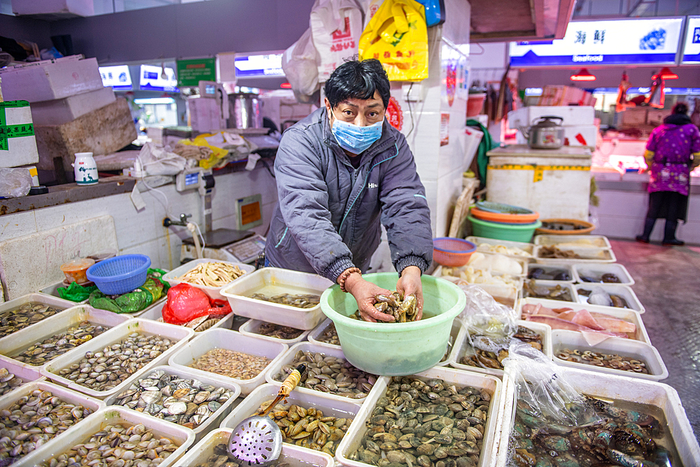 Shanghai, China, 26th Jan 2020, A store vendor wearing a masks handles shellfish with hands at seafood market