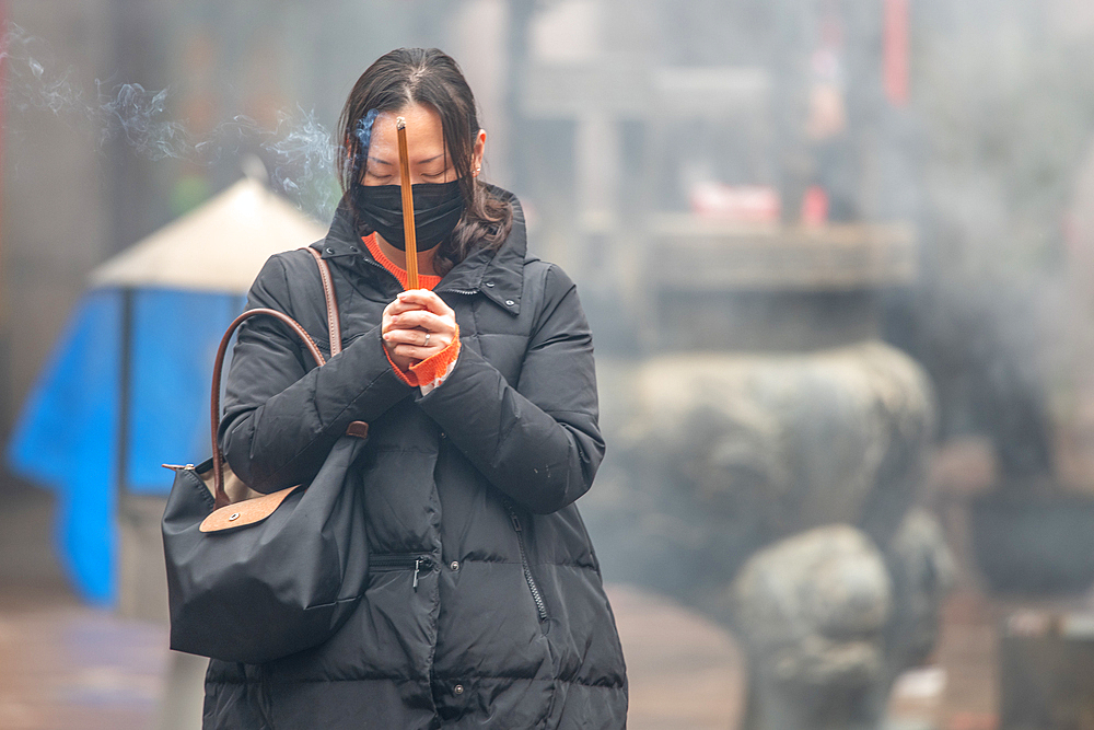 Shanghai, China, 23rd Jan 2020, A woman wearing a mask prays with burning joss sticks